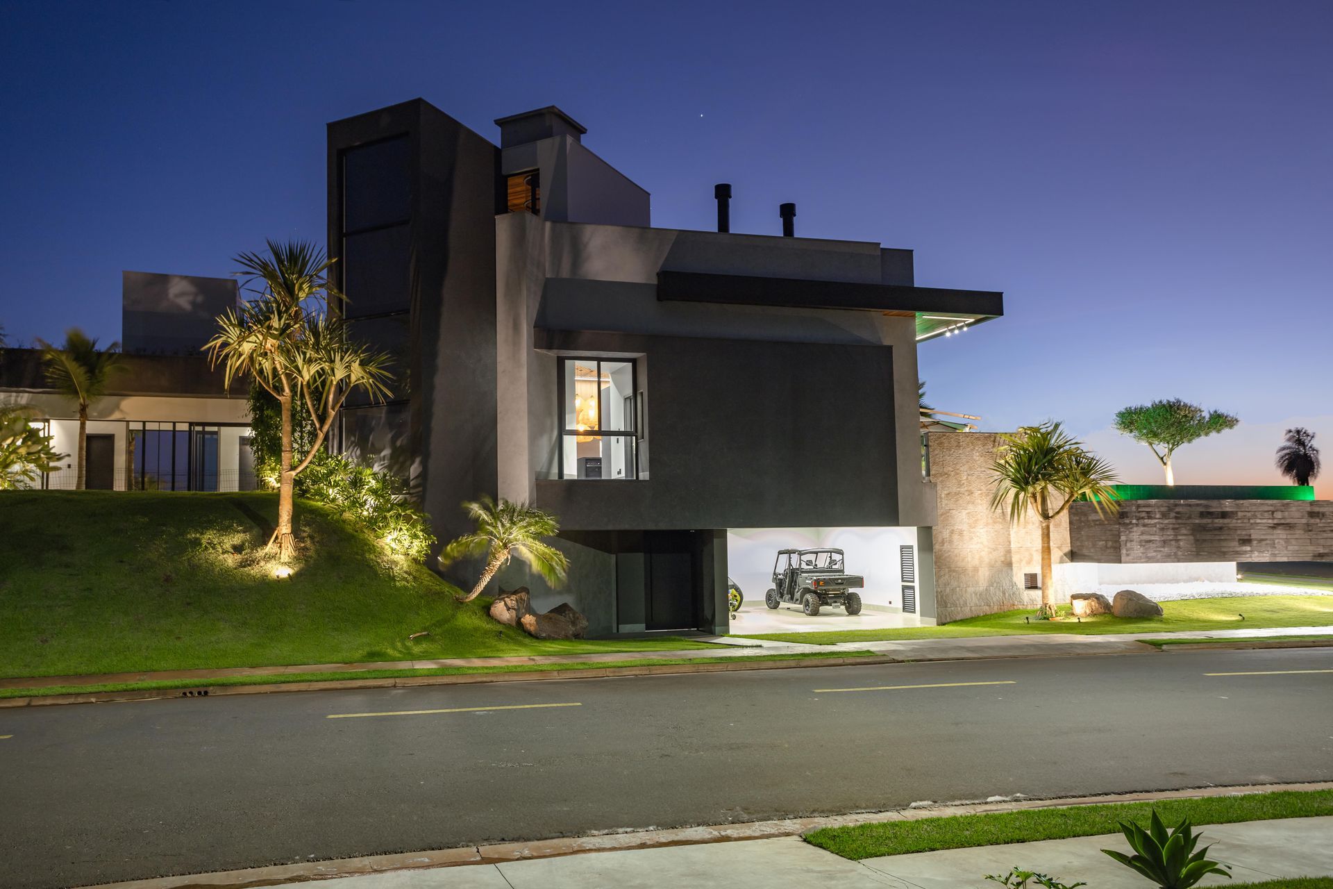 Casa cinza moderna à noite com gramado e rua.