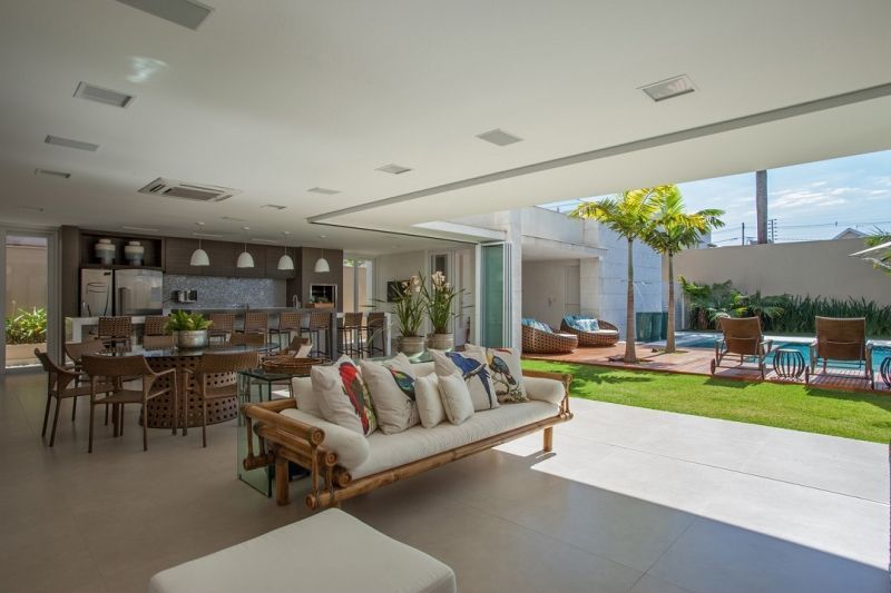 Sala de estar em conceito aberto com sofá de bambu, mesa de jantar e cozinha; acesso a um quintal com piscina.