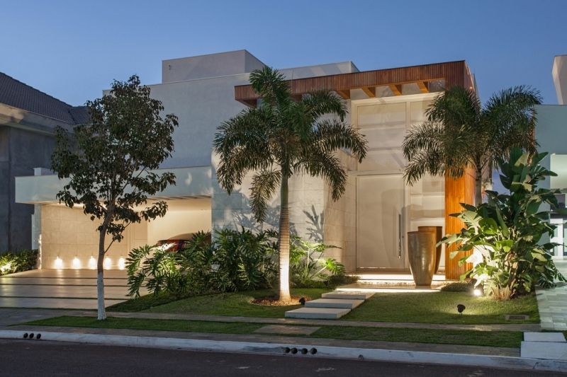 Exterior de uma casa moderna ao entardecer com palmeiras e iluminação paisagística.