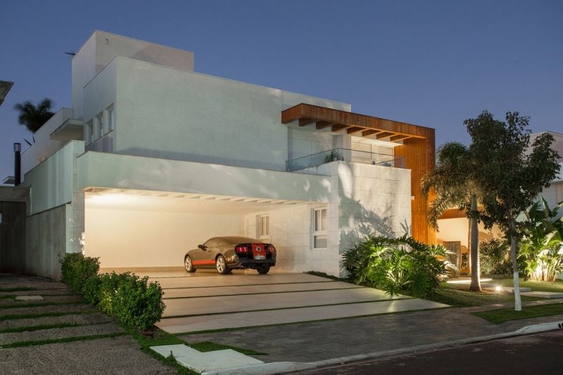 Casa branca moderna com carro na garagem ao anoitecer, vegetação exuberante.
