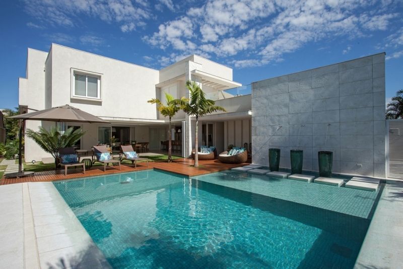 Casa branca moderna com piscina e assentos ao ar livre sob um céu azul brilhante.