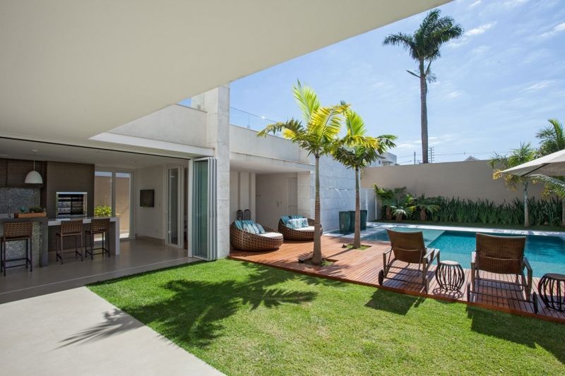 Quintal com piscina, gramado, espreguiçadeiras e cozinha; dia ensolarado.