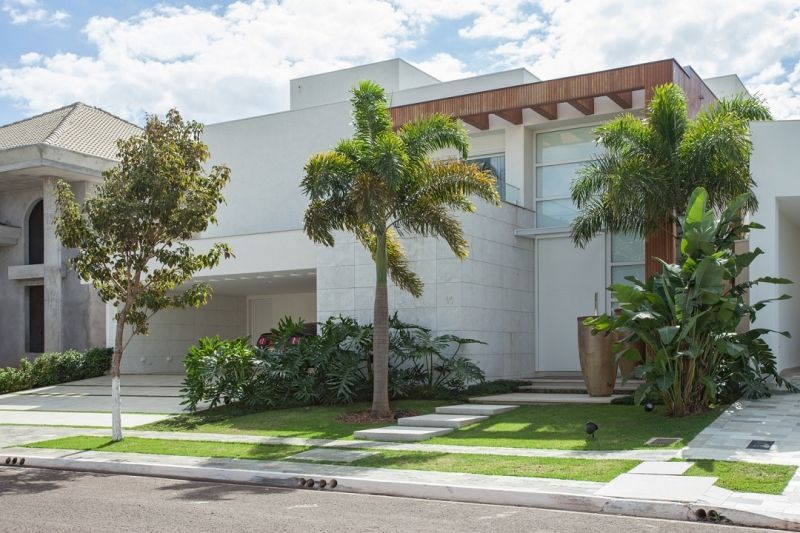 Casa branca moderna com uma palmeira e grama verde na frente.