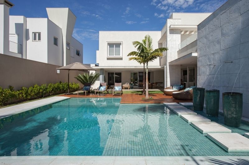 Uma casa branca moderna com piscina, um pátio e uma pequena palmeira.