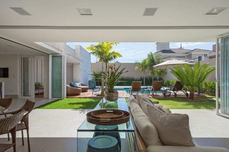 Vista luxuosa do quintal: piscina, móveis de sala, gramado verde, portas abertas da sala de estar.