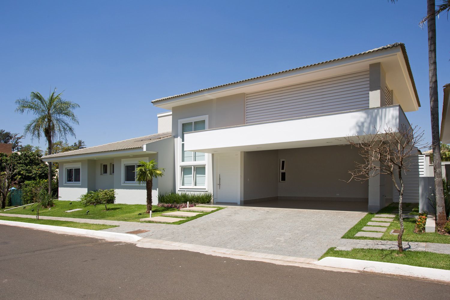 Casa moderna de dois andares com revestimento cinza e uma garagem coberta, em um dia ensolarado.