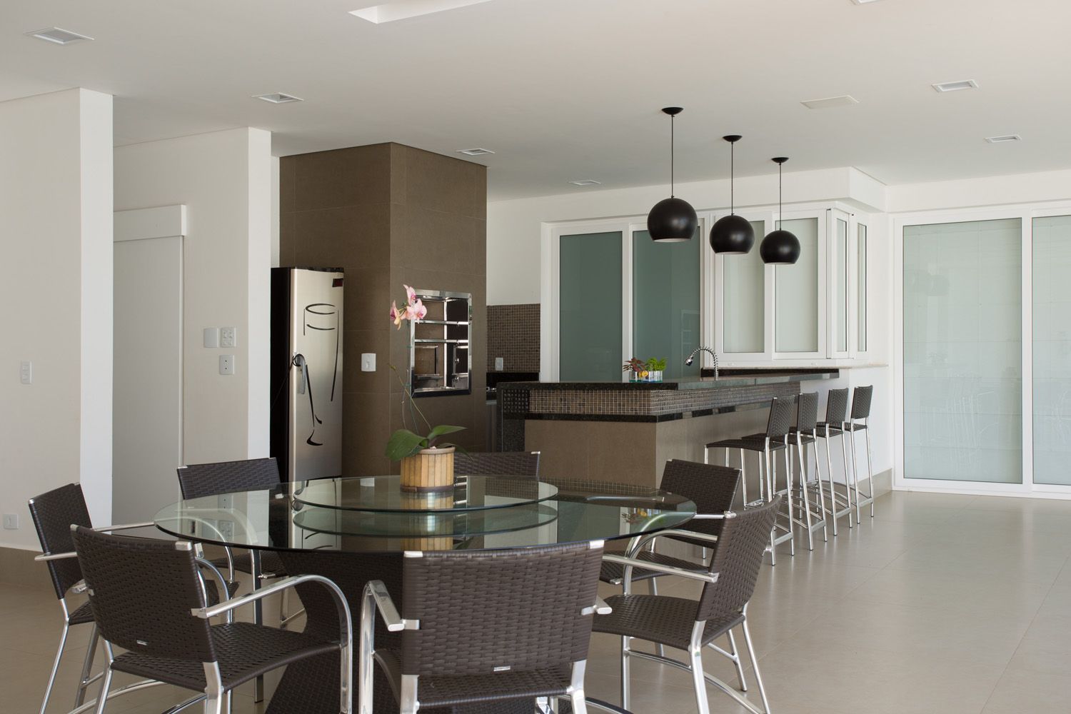 Sala de jantar moderna com mesa de vidro, cadeiras e uma ilha de cozinha com bancos de bar.