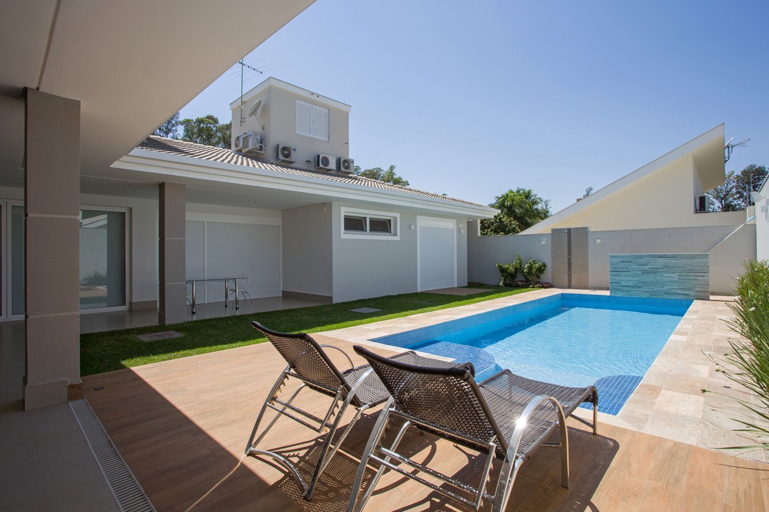 Duas espreguiçadeiras de vime ficam de frente para uma piscina retangular no quintal.