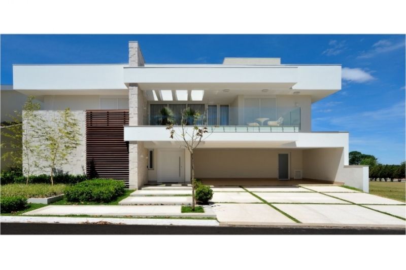 Casa moderna branca de dois andares com janelas grandes, garagem coberta e entrada de concreto.