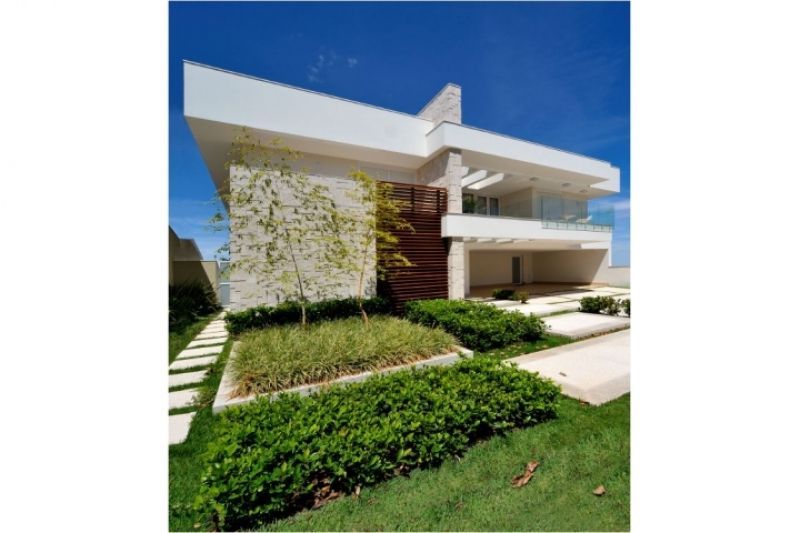 Casa branca moderna com paisagismo e céu azul.