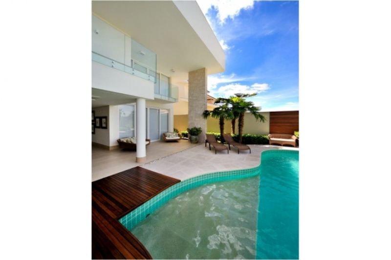 Exterior de casa moderna com piscina, pátio e palmeiras sob um céu azul.