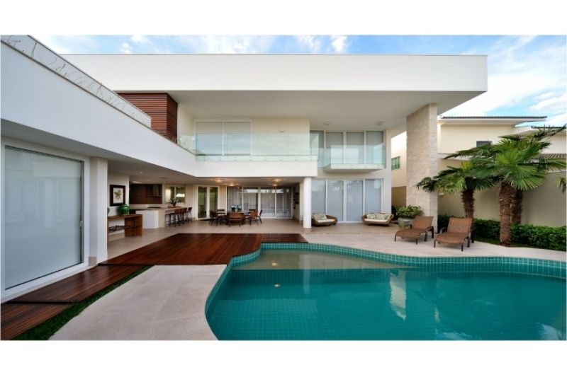 Casa moderna e luxuosa com piscina, pátio e área de estar ao ar livre. Exterior em tons de branco e marrom, com palmeira.