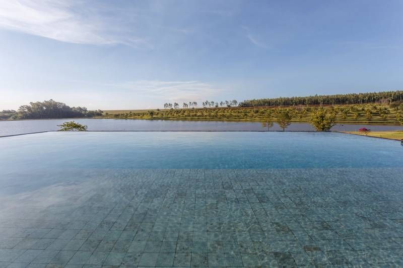 Piscina de borda infinita com vista para um lago sereno sob um céu azul, com árvores ao longe.