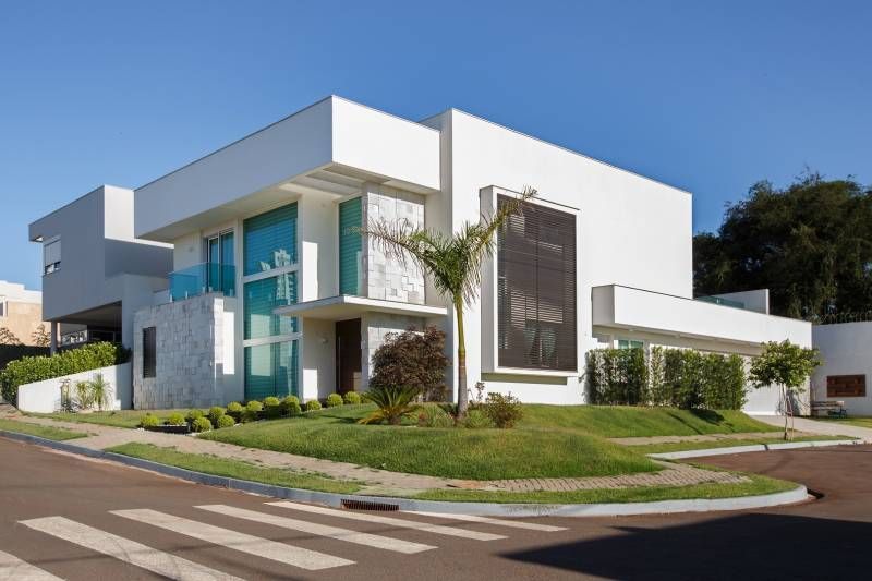 Casa branca moderna com grandes janelas, detalhes em azul e gramado bem cuidado em um dia ensolarado.
