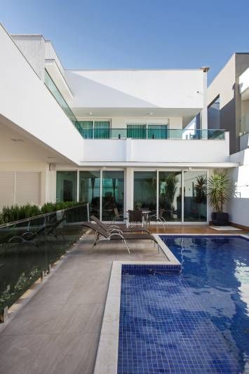 Casa branca moderna com piscina e pátio. Água azul, janelas de vidro verde e céu limpo.