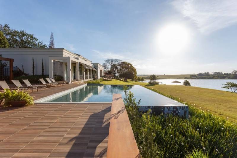 Uma luxuosa piscina ao ar livre ao lado de um lago e um moderno edifício branco em um dia ensolarado.