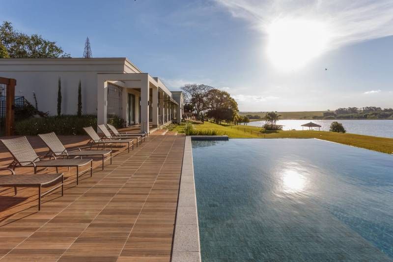 Luxo à beira do lago: piscina com espreguiçadeiras, edifício moderno e ensolarado com vista.