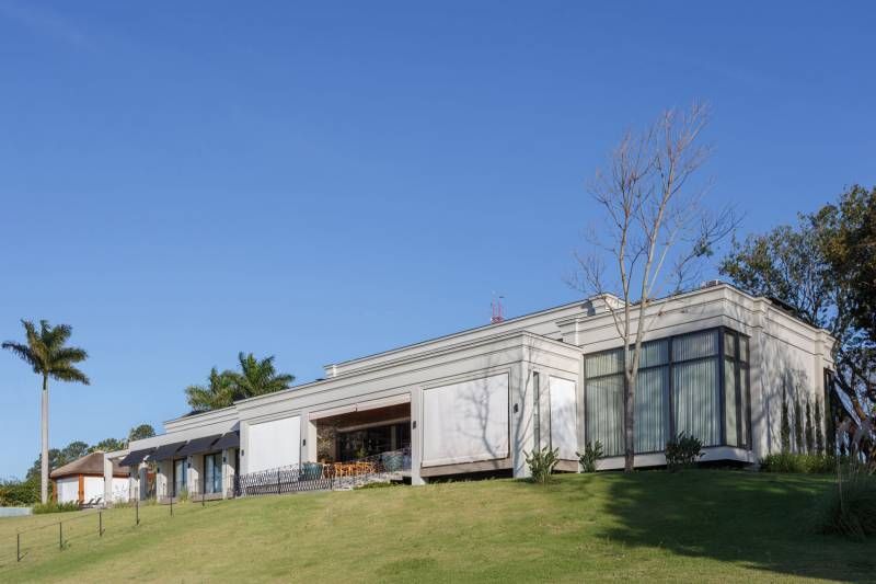 Edifício branco moderno com grandes janelas em uma colina gramada sob um céu azul.