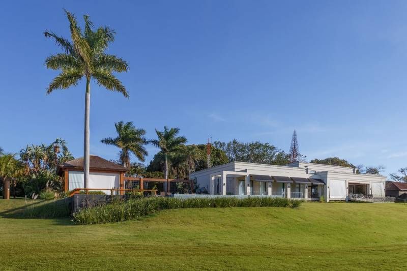 Uma casa branca moderna com piscina, palmeiras e um gramado verde sob um céu azul.