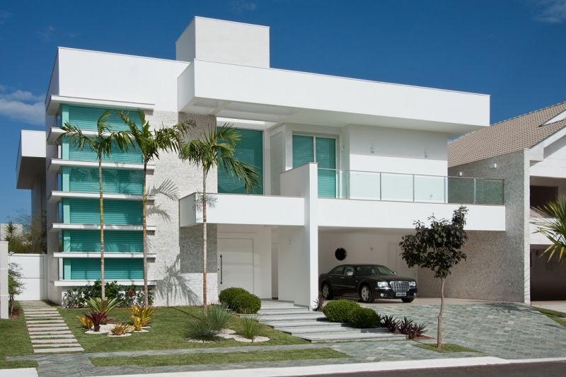 Casa branca moderna com janelas azul-petróleo e um carro na garagem.