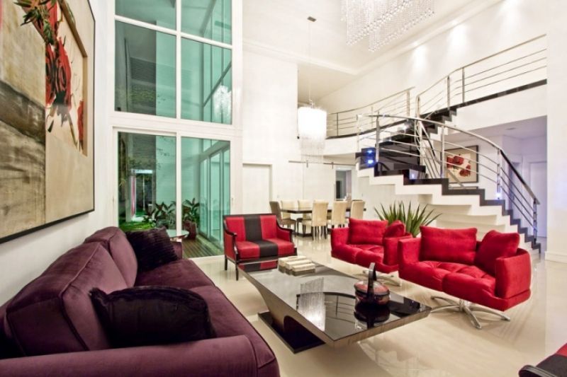Sala de estar moderna com móveis vermelhos e roxos, paredes brancas e uma escada.