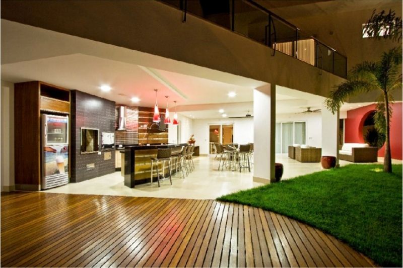 Casa moderna de conceito aberto com sala de estar interna e externa. Cozinha com bar, deck de madeira, gramado e varanda no segundo andar.