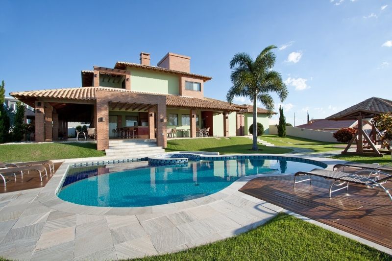 Casa com piscina. Paredes verdes, telhado de telhas vermelhas, água azul, palmeira, dia ensolarado.