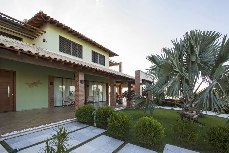 Casa de dois andares com fachada verde, telhado marrom e um quintal verde com uma palmeira.