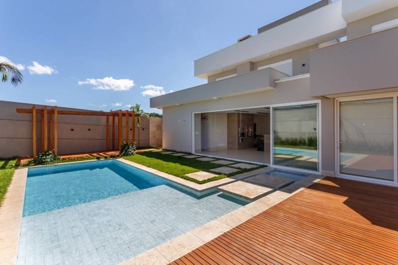 Casa moderna com piscina, deck de madeira e portas de vidro deslizantes; dia ensolarado.