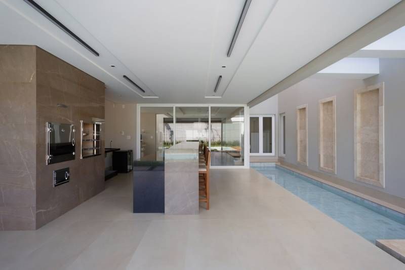 Cozinha externa moderna com churrasqueira embutida, assentos de bar e um espelho d'água na lateral.