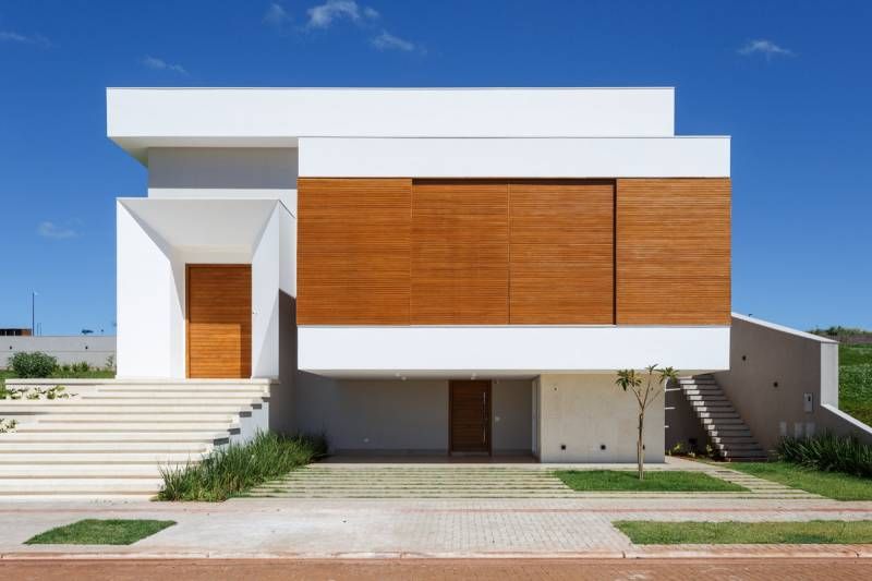 Casa branca moderna com painéis de madeira, degraus e um céu azul claro.
