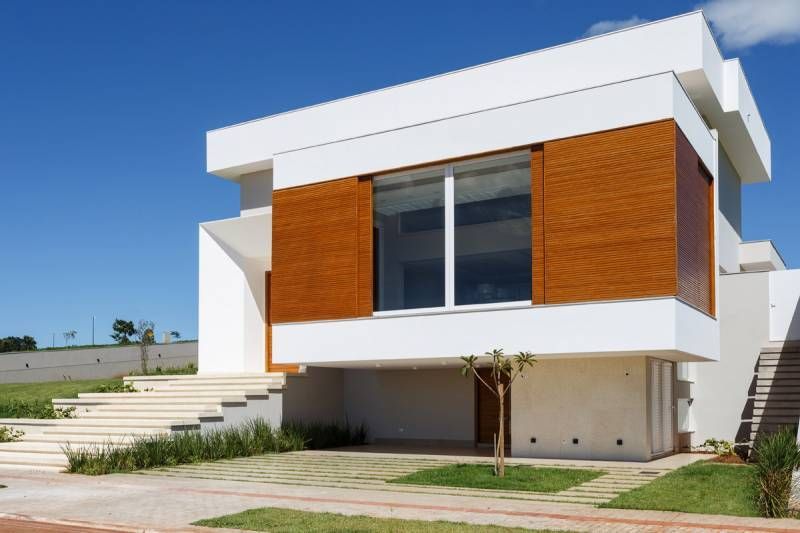 Casa branca moderna com janelas com painéis de madeira, escadas que levam até o topo e um céu azul.