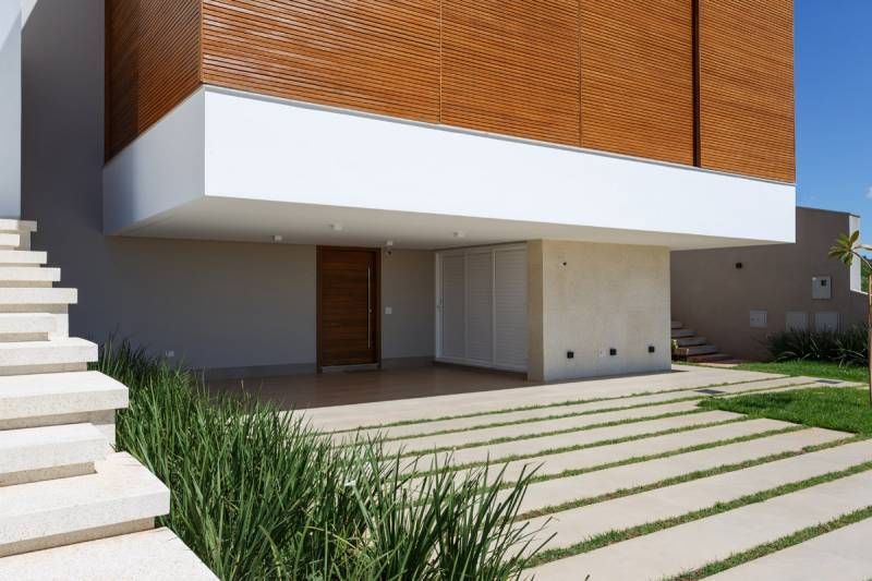 Exterior de uma casa moderna com fachada de madeira, detalhes em branco, degraus de concreto e entrada de automóveis.