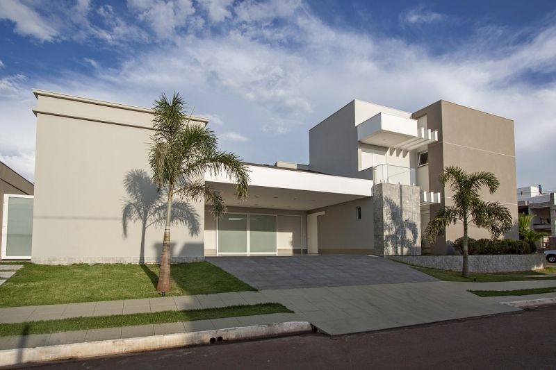 Casa moderna com cores neutras, calçada, palmeiras e céu azul.
