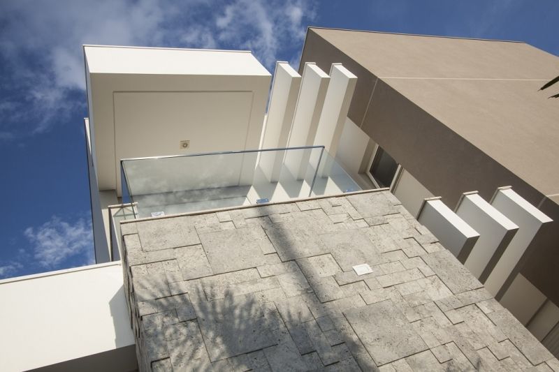 Edifício moderno com fachada de pedra e branca, varanda de vidro, céu azul.
