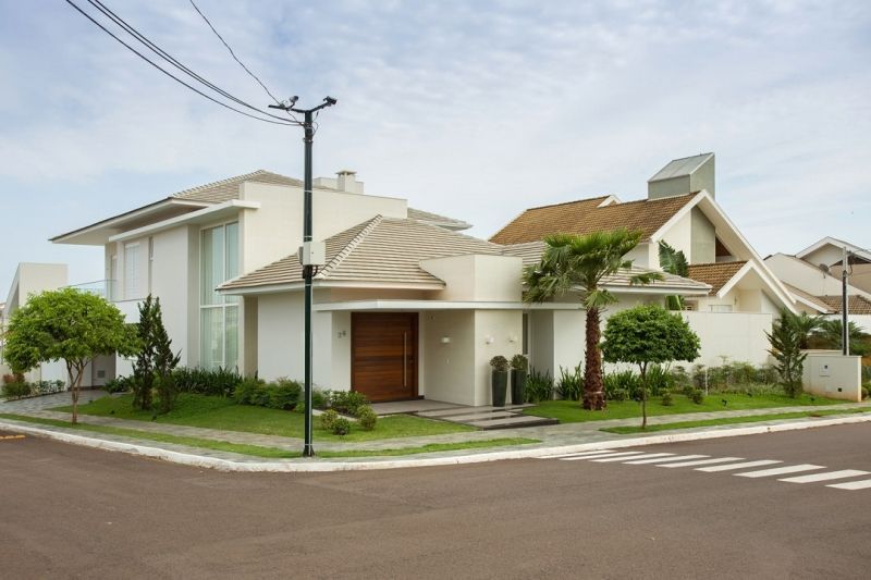 Casa moderna branca em um lote de esquina com telhado e calçada marrom claro.