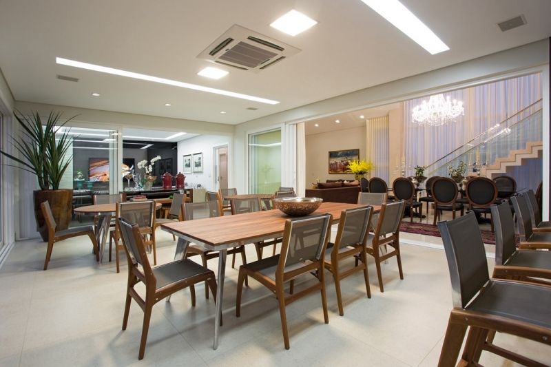 Ampla sala de jantar com mesas de madeira, cadeiras e vista para outra sala com escadas e móveis.