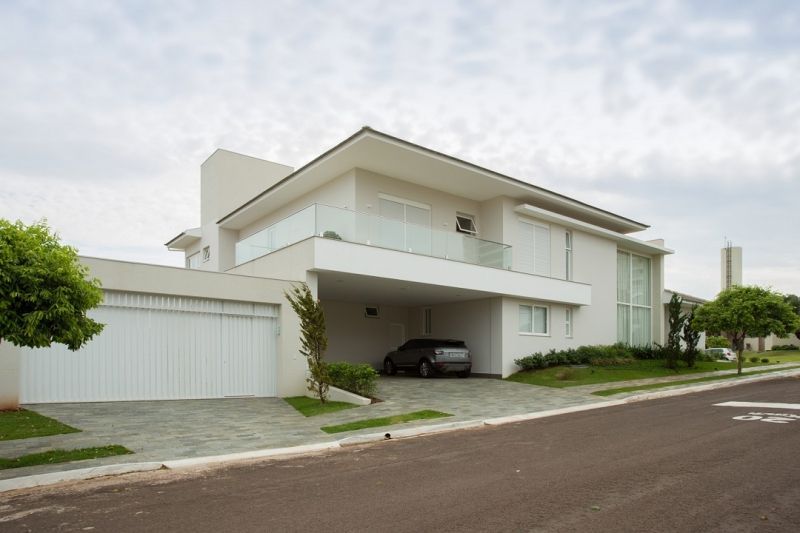 Casa branca moderna com garagem e carro anexos, em uma rua suburbana.
