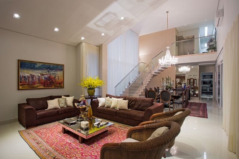 Sala de estar com escada e área de jantar, com sofás marrons, um tapete rosa e um lustre.