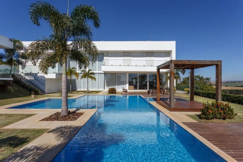 Casa branca moderna com piscina e pérgola de madeira em um dia ensolarado.