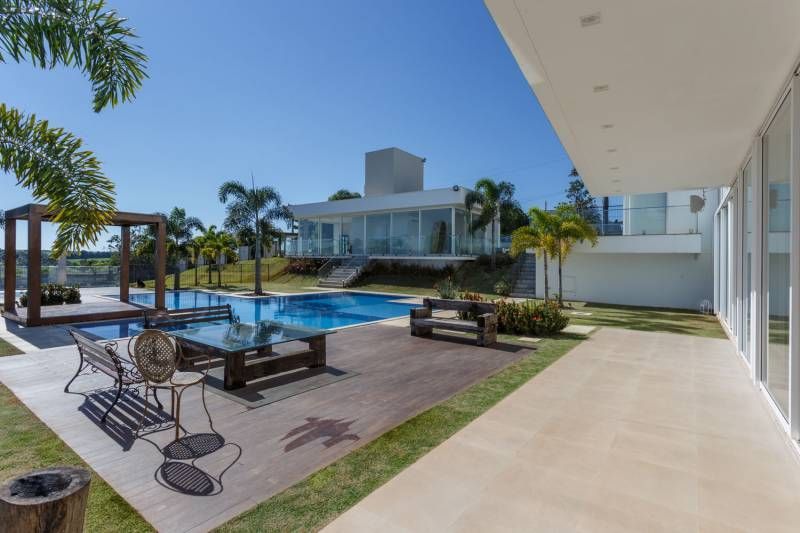 Casa luxuosa com piscina, móveis de jardim e um moderno edifício branco sob um céu azul brilhante.