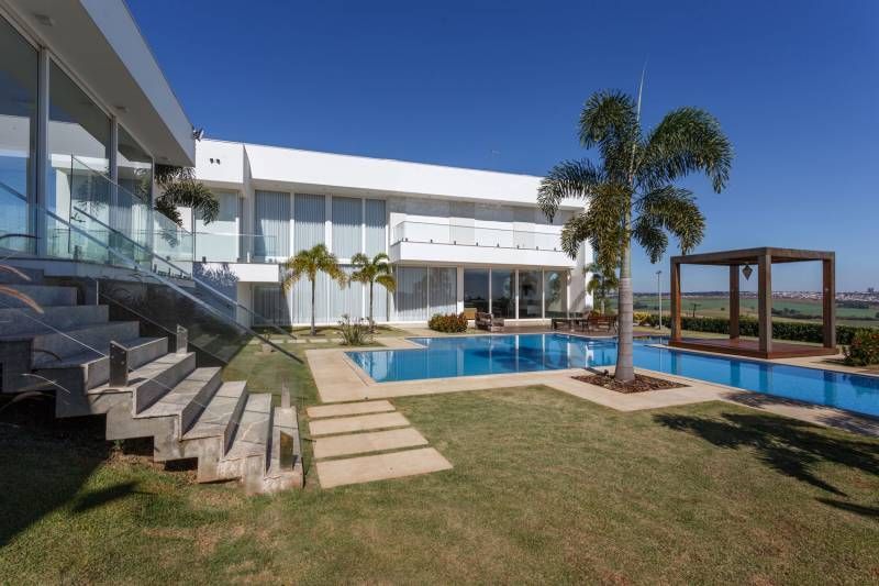 Casa branca moderna com piscina, palmeiras e gazebo em um dia ensolarado.