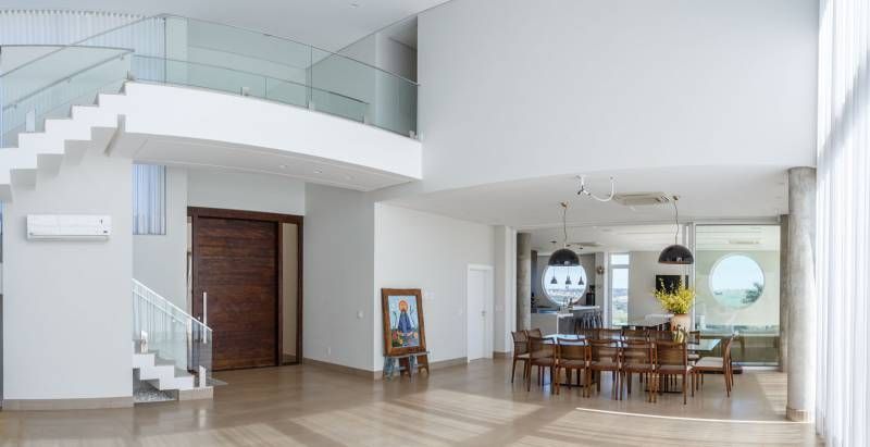 Interior espaçoso e iluminado, com escada, mesa de jantar e retrato. Janelas amplas, cores neutras.