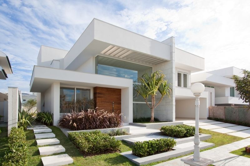 Casa branca moderna com porta de madeira, janelas de vidro e jardim paisagístico na frente.