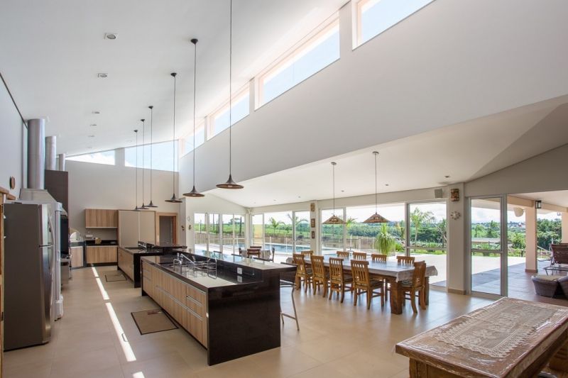 Cozinha/sala de jantar em conceito aberto com uma grande ilha, mesa de madeira e janelas amplas com vista para um pátio e paisagem.