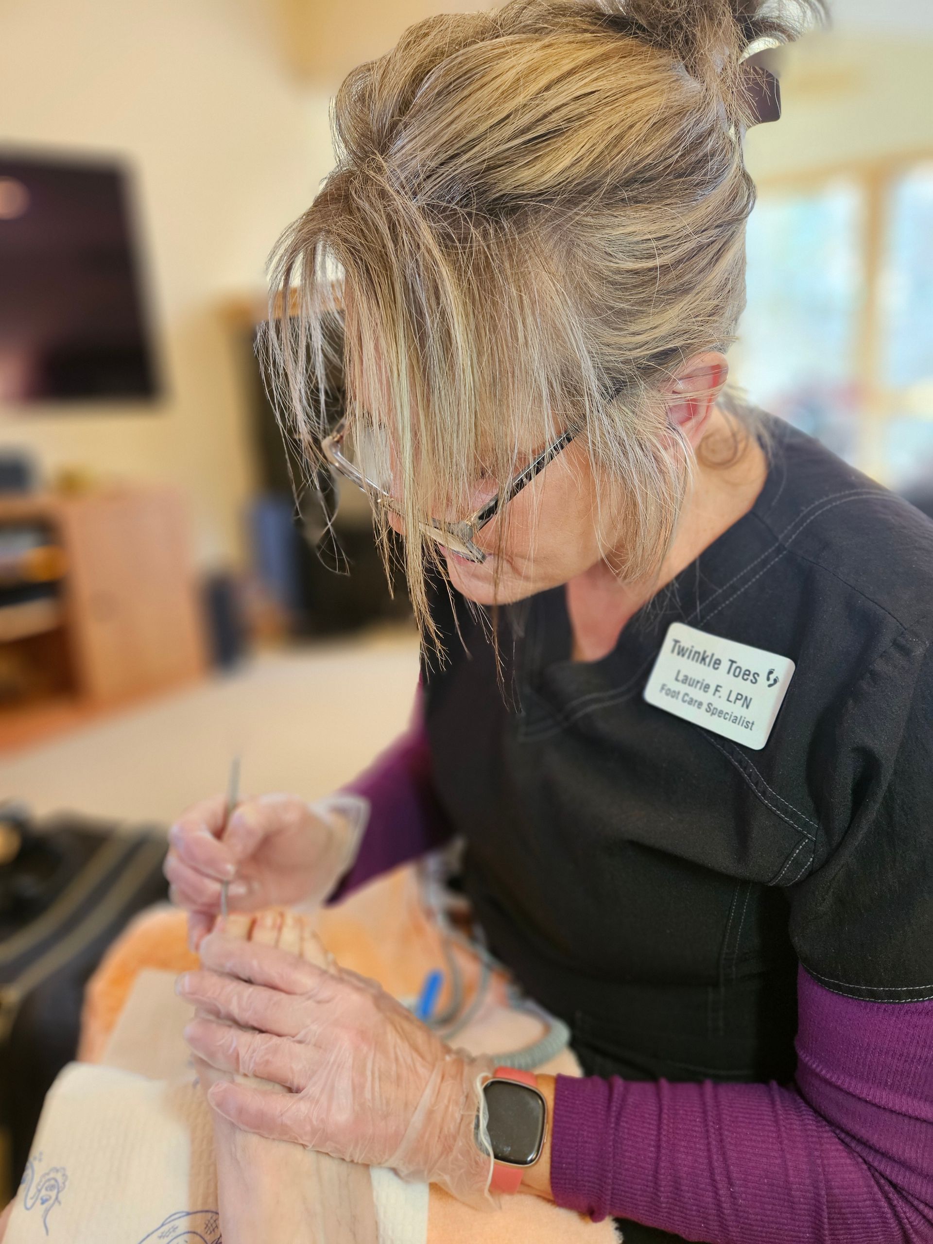 A professional in scrubs wears gloves and uses a tool to perform a foot care procedure on a patient.