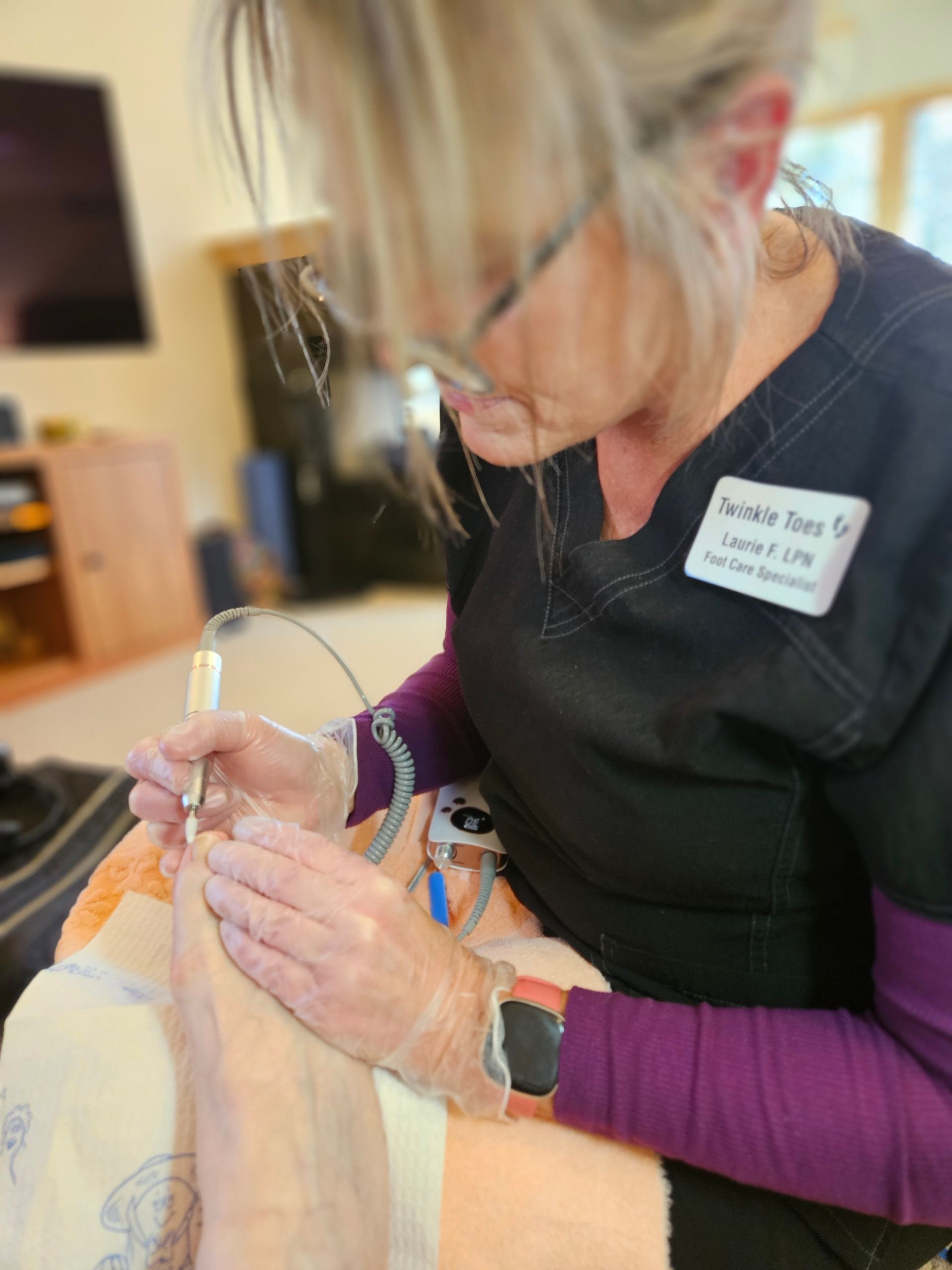 A medical professional wearing gloves performs a nail procedure on a patient's foot using a handheld electric device.