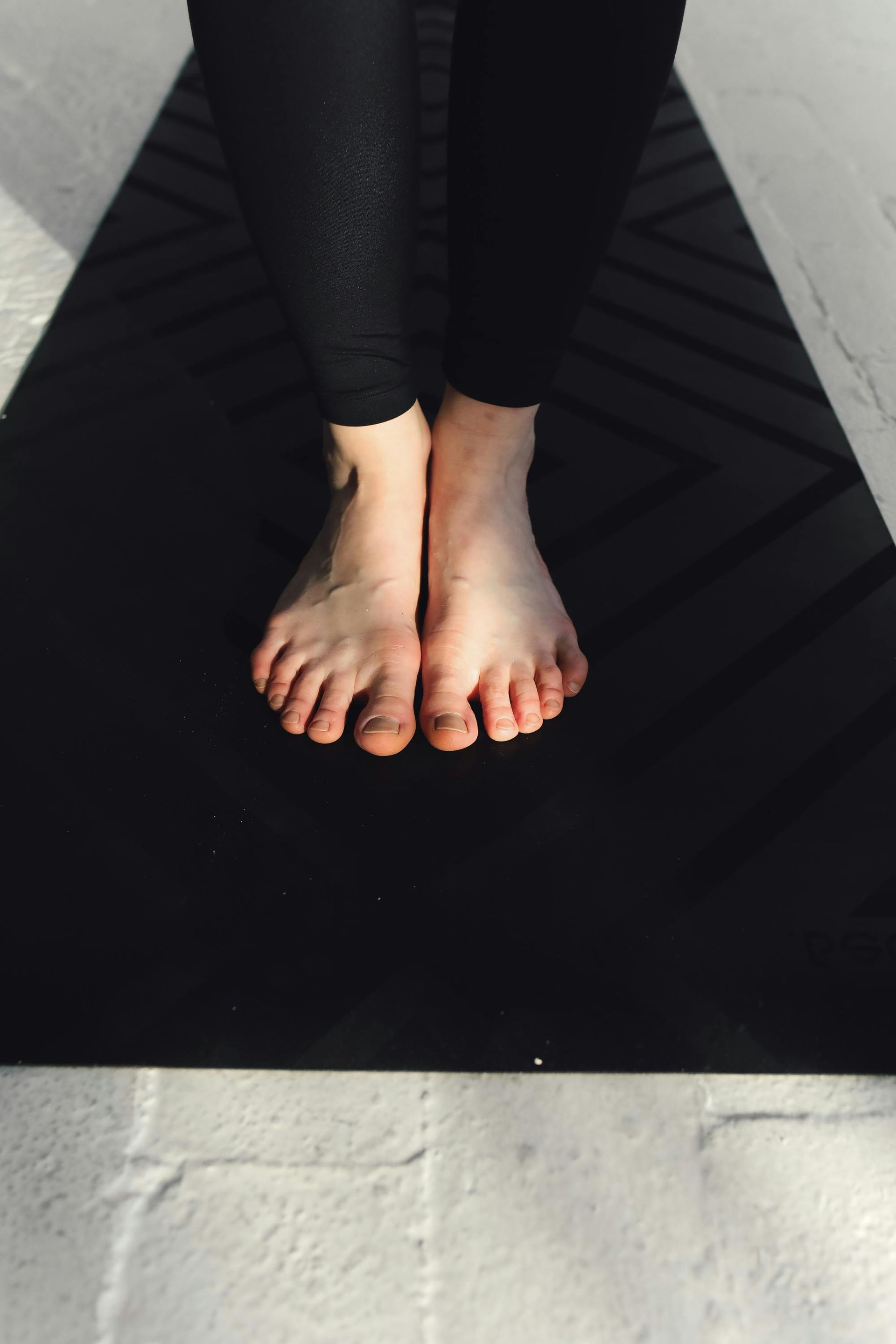 Bare feet on a black yoga mat, legs in dark leggings. Bright sunlight.