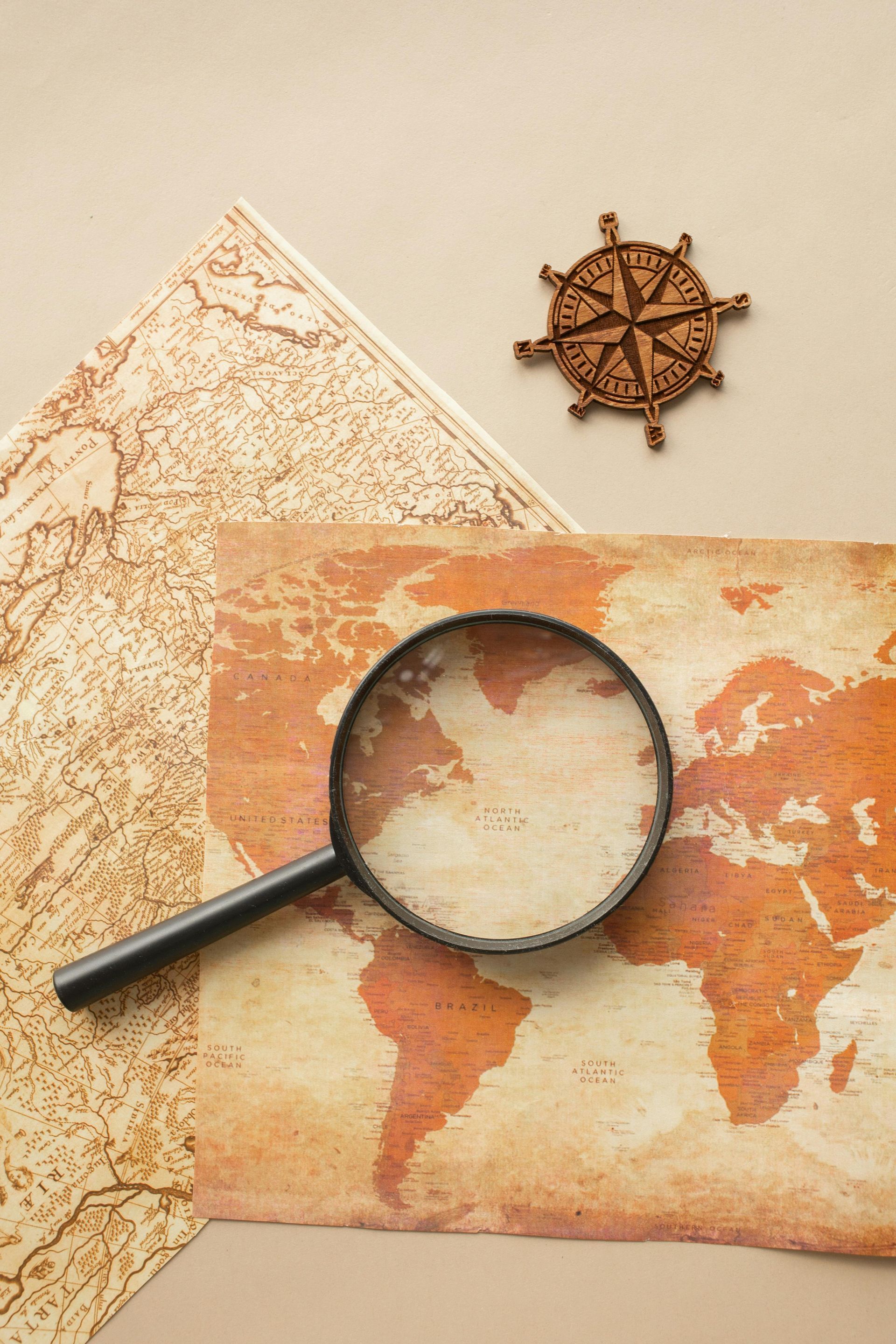 Magnifying glass over a world map with a compass rose, on a beige background.
