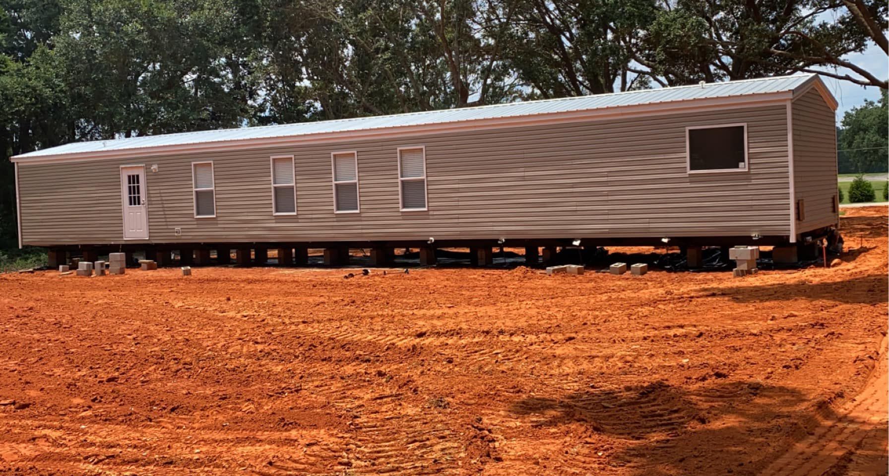 A mobile home is sitting in the middle of a dirt field.